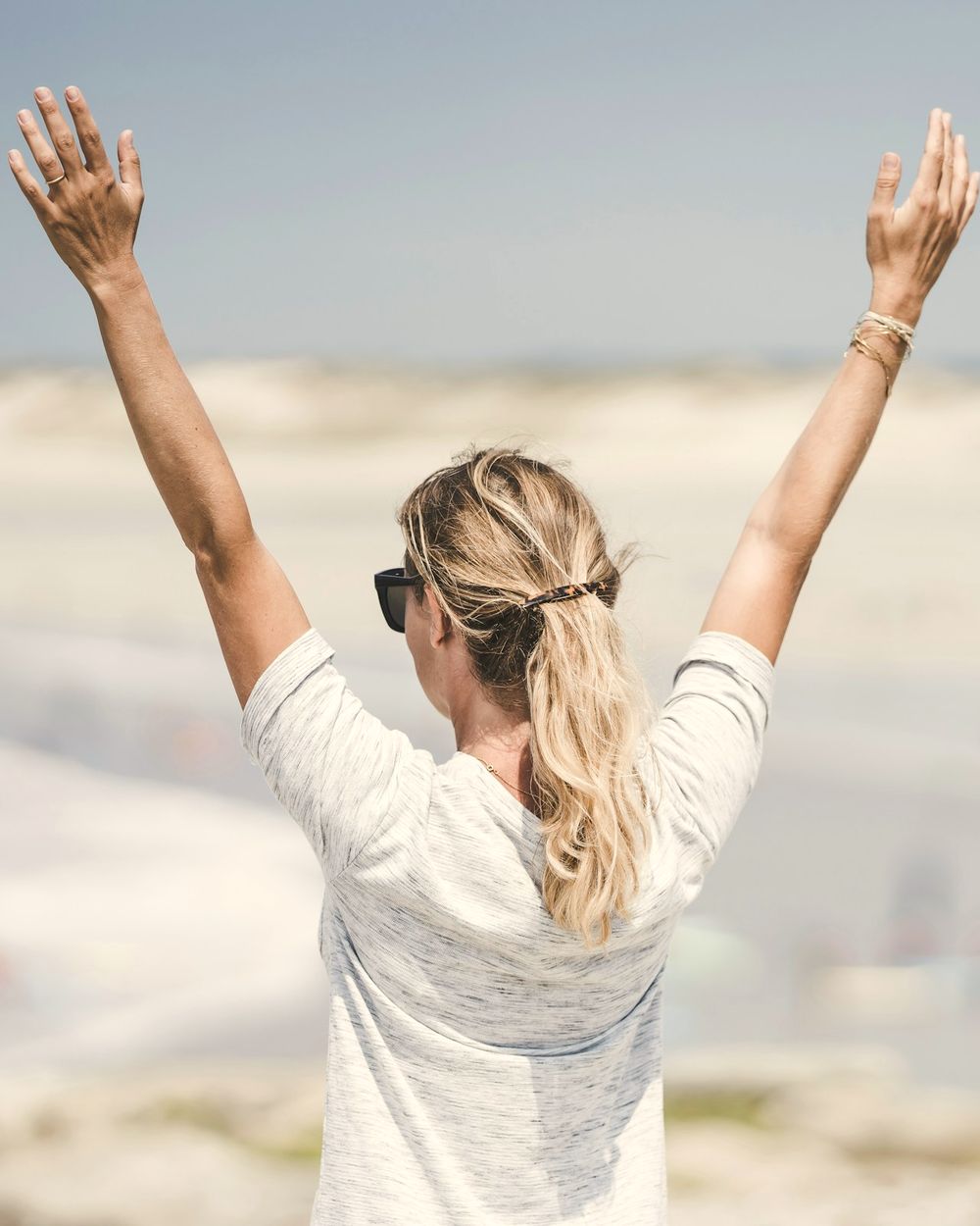 Una donna di spalle alza le braccia al cielo, in riva al mare